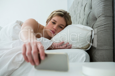 Young woman waking up with mobile alarm clock