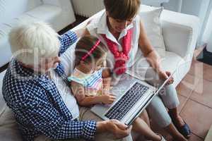 Grandparents and granddaughter using laptop in living room