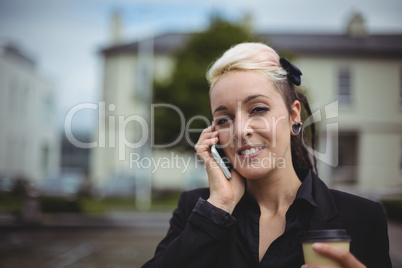 Portrait of businesswoman talking on mobile phone while holding disposable coffee cup