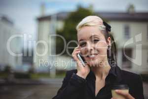 Portrait of businesswoman talking on mobile phone while holding disposable coffee cup