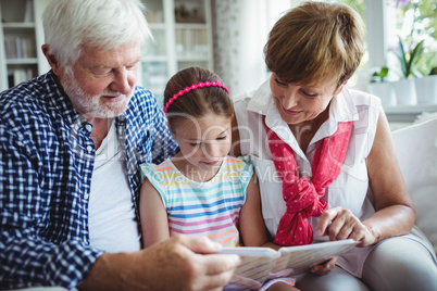 Grandparents and grand daughter looking at photo album in living room
