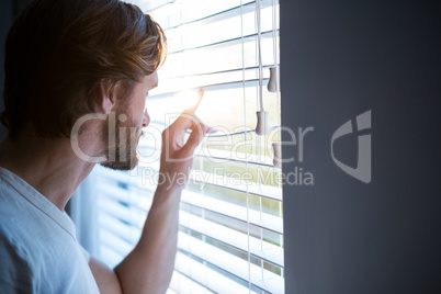 Man looking through window blinds after waking up