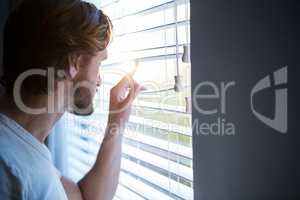 Man looking through window blinds after waking up