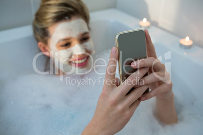 Woman using mobile phone while having bath in bathtub