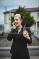 Businesswoman talking on mobile phone while holding disposable coffee cup