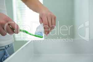Woman putting toothpaste on brush in bathroom