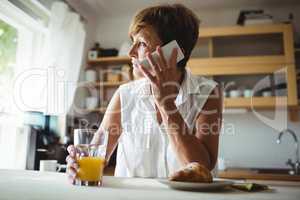 Senior woman talking on phone while having breakfast