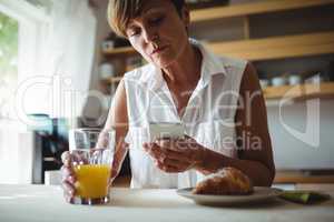 Senior woman using mobile phone while having breakfast