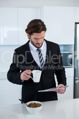 Businessman reading newspaper while having coffee in kitchen