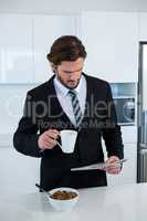 Businessman reading newspaper while having coffee in kitchen
