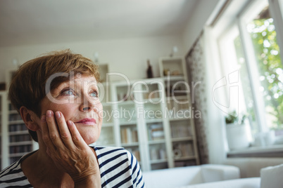 Thoughtful senior woman sitting on sofa in living room