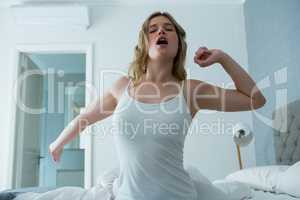 Young woman waking up in bed and stretching her arms