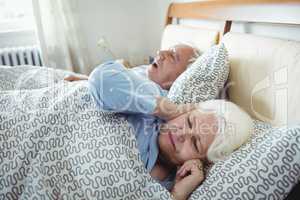 Man snoring and woman covering her ears while sleeping on bed