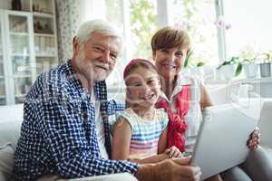 Grandparents and granddaughter using laptop in living room
