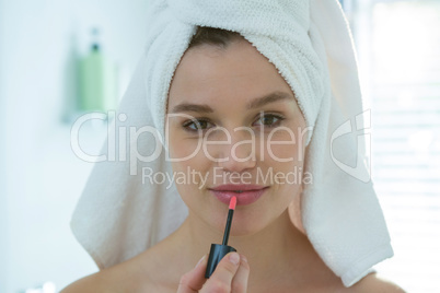 Woman applying lip gloss on her lips in bathroom