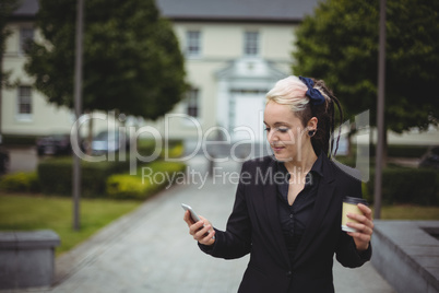 Businesswoman using mobile phone while holding disposable coffee cup