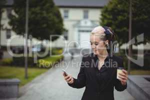 Businesswoman using mobile phone while holding disposable coffee cup