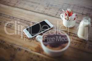 Close-up of coffee cup with mobile phone and milk bottle