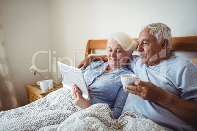 Senior woman using digital tablet and man having cup of coffee