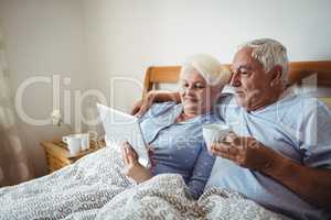 Senior woman using digital tablet and man having cup of coffee