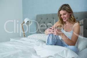 Smiling woman using mobile phone on bed