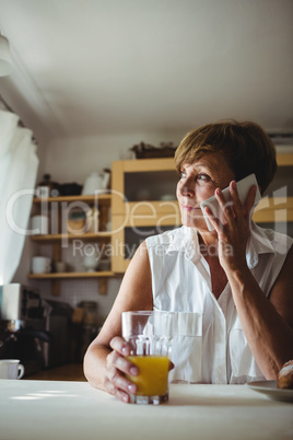 Senior woman talking on phone while having breakfast