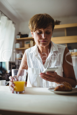 Senior woman using mobile phone while having breakfast