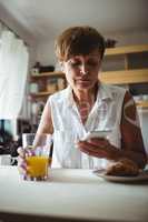 Senior woman using mobile phone while having breakfast