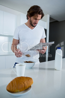 Man reading newspaper while having breakfast in kitchen