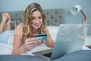 Woman doing online shopping with her laptop on bed