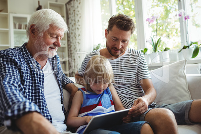 Boy using digital tablet with his father and grandfather in living room