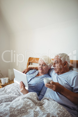 Senior woman using digital tablet and man having cup of coffee