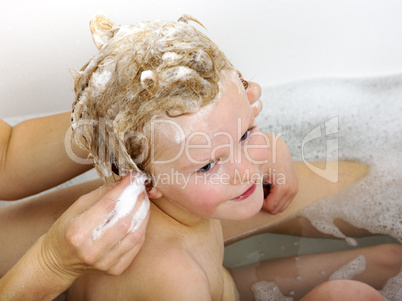 Child sits in the bath with the hair wash