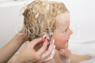 Child sits in the bath with the hair wash