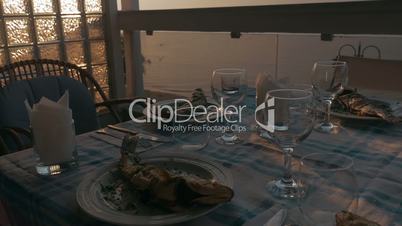 At sunset in city of Perea, Greece, dinner table served with cooked fish