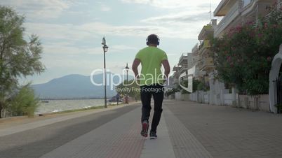 Young man in headphones runs on road of city Perea, Greece
