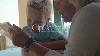 In city of Perea, Greece sits a grandmother with her grandson and teaches him how use tablet