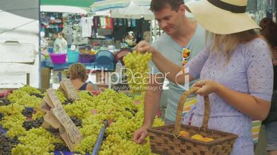 couple choosing grapes and speaking with smile on outdoor market. Thessaloniki, Greece