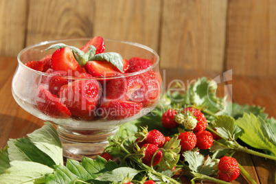 ripe strawberries in a transparent bowl and bunches with leaves