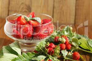 ripe strawberries in a transparent bowl and bunches with leaves