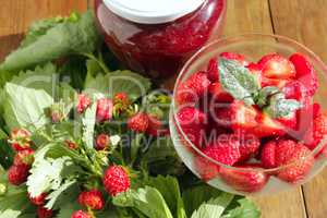 ripe strawberries in a transparent bowl and bunches with leaves