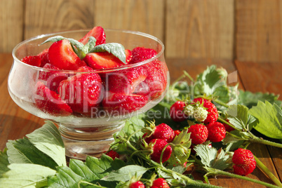 ripe strawberries in a transparent bowl and bunches with leaves