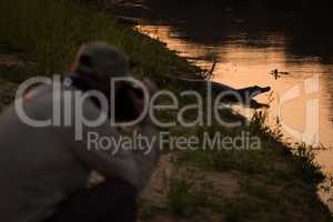 Photographer shooting yacare caiman on river bank