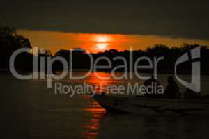 Sun setting over silhouetted boat on river