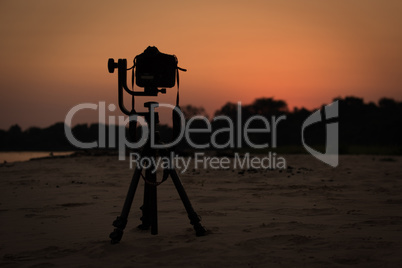 Camera on tripod by river at sunset