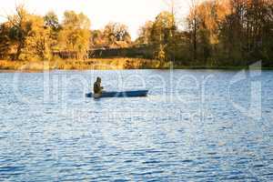 Autumn landscape: the lake and the fisherman on the boat.