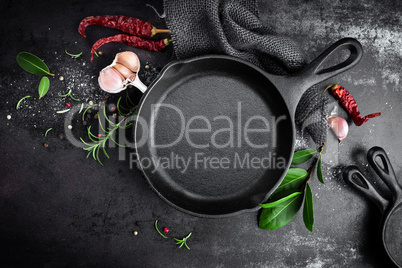 cast iron pan and spices on black metal culinary background, view from above