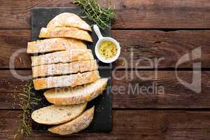 fresh homemade ciabatta bread sliced on stone slate board, olive oil and rosemary on wooden background