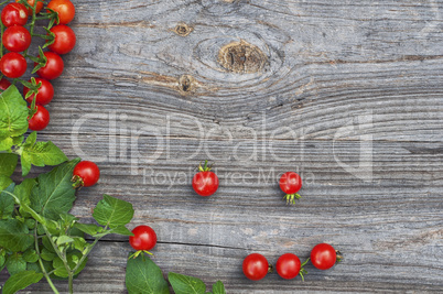 Red small tomatoes cherry with leaves on a wooden surface