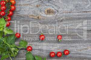 Red small tomatoes cherry with leaves on a wooden surface